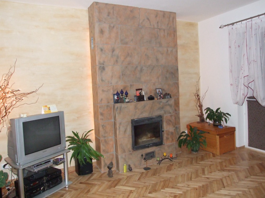 Wykończony salon z obudowanym kominkiem z płytek imitujących kamień, dekoracyjną ścianą, telewizorem i parkietem w jodełkę.